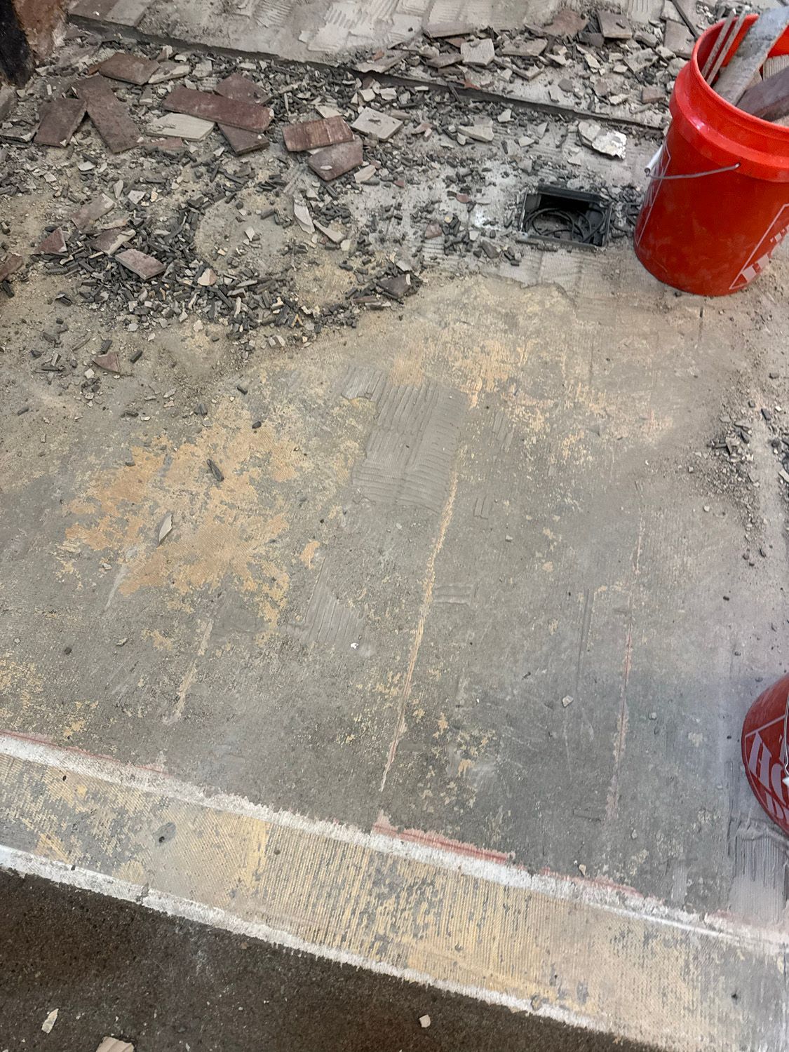 Close-up of cracked concrete pavement with a red bucket at the top right and a white curb line near the bottom.