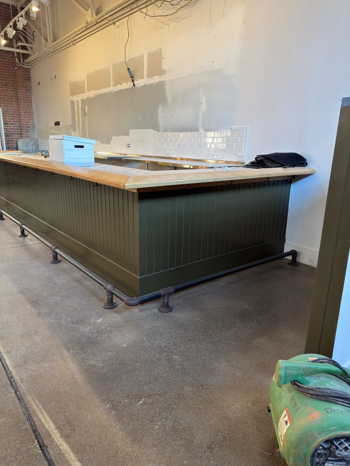 Empty restaurant counter with a wooden top, dark green base, and a small blue box on it.