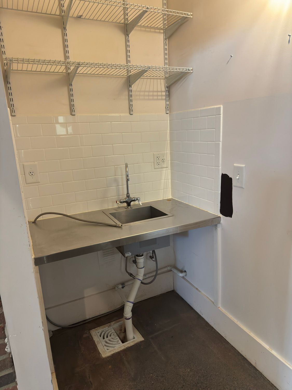 Small utility sink with stainless counter, white tile backsplash, and open shelves in a compact laundry room
