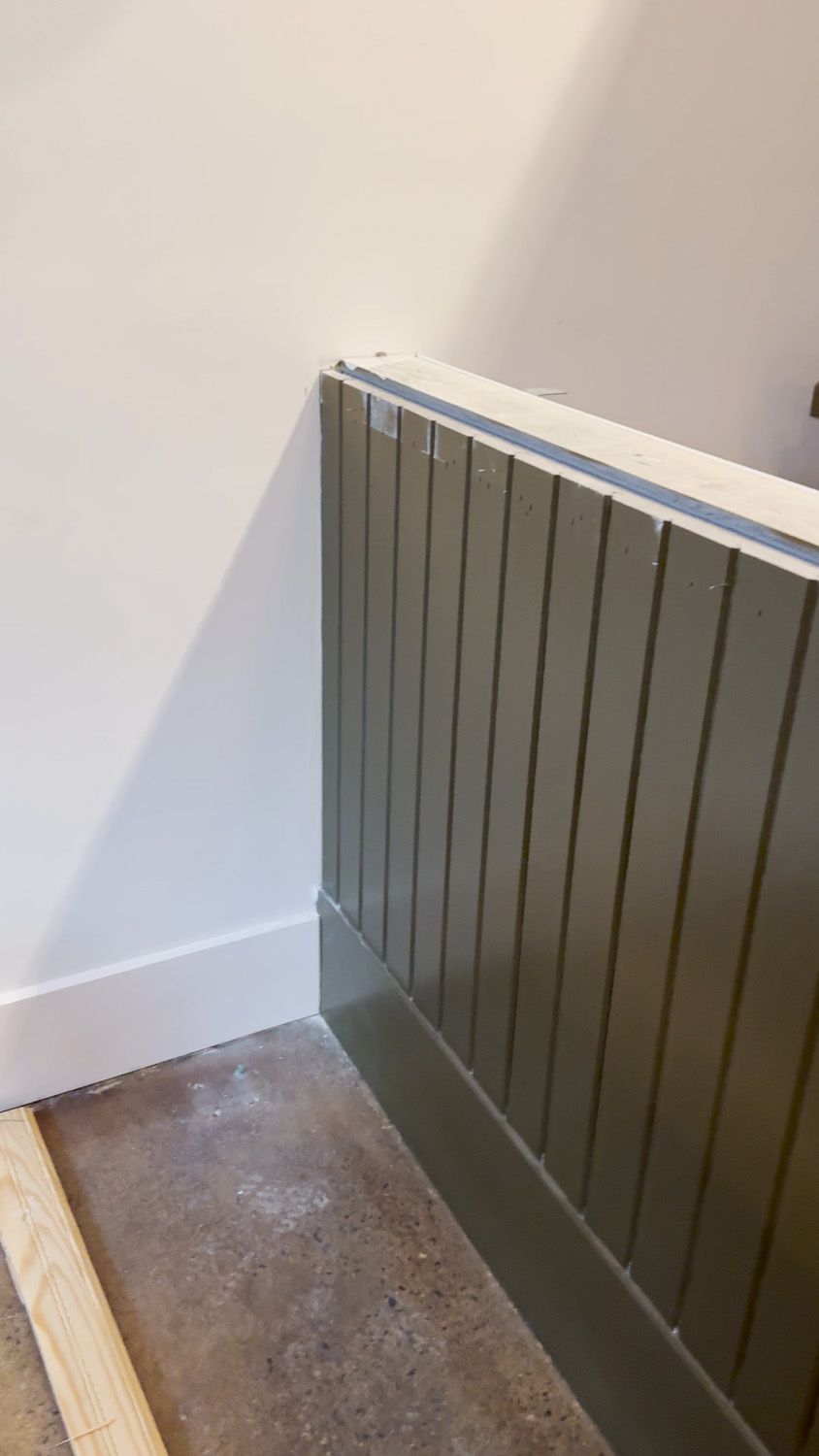 Gray slatted radiator cover against a white wall beside a worn concrete floor.