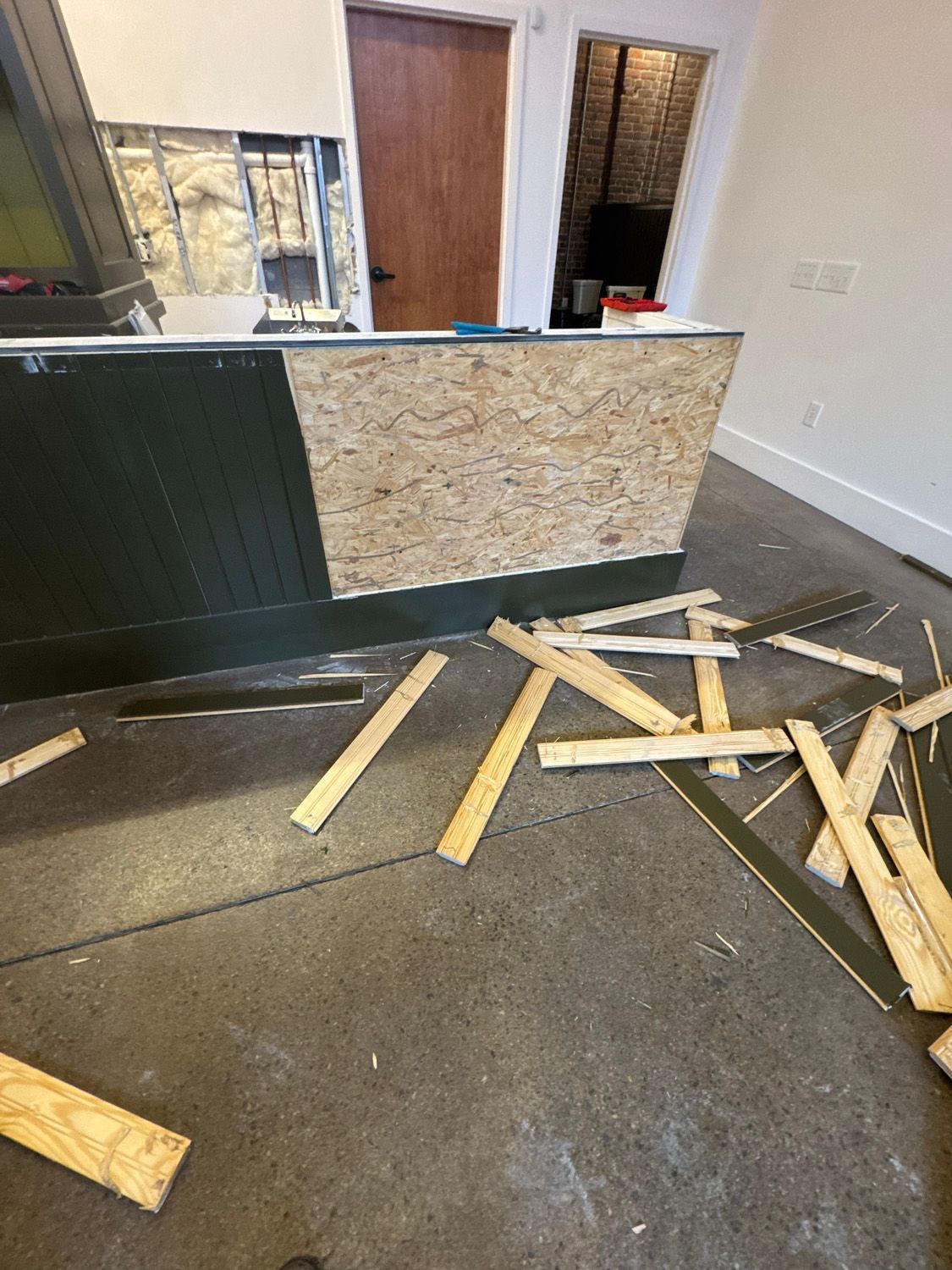 Messy room with scattered wood scraps on the floor beside a counter and window area