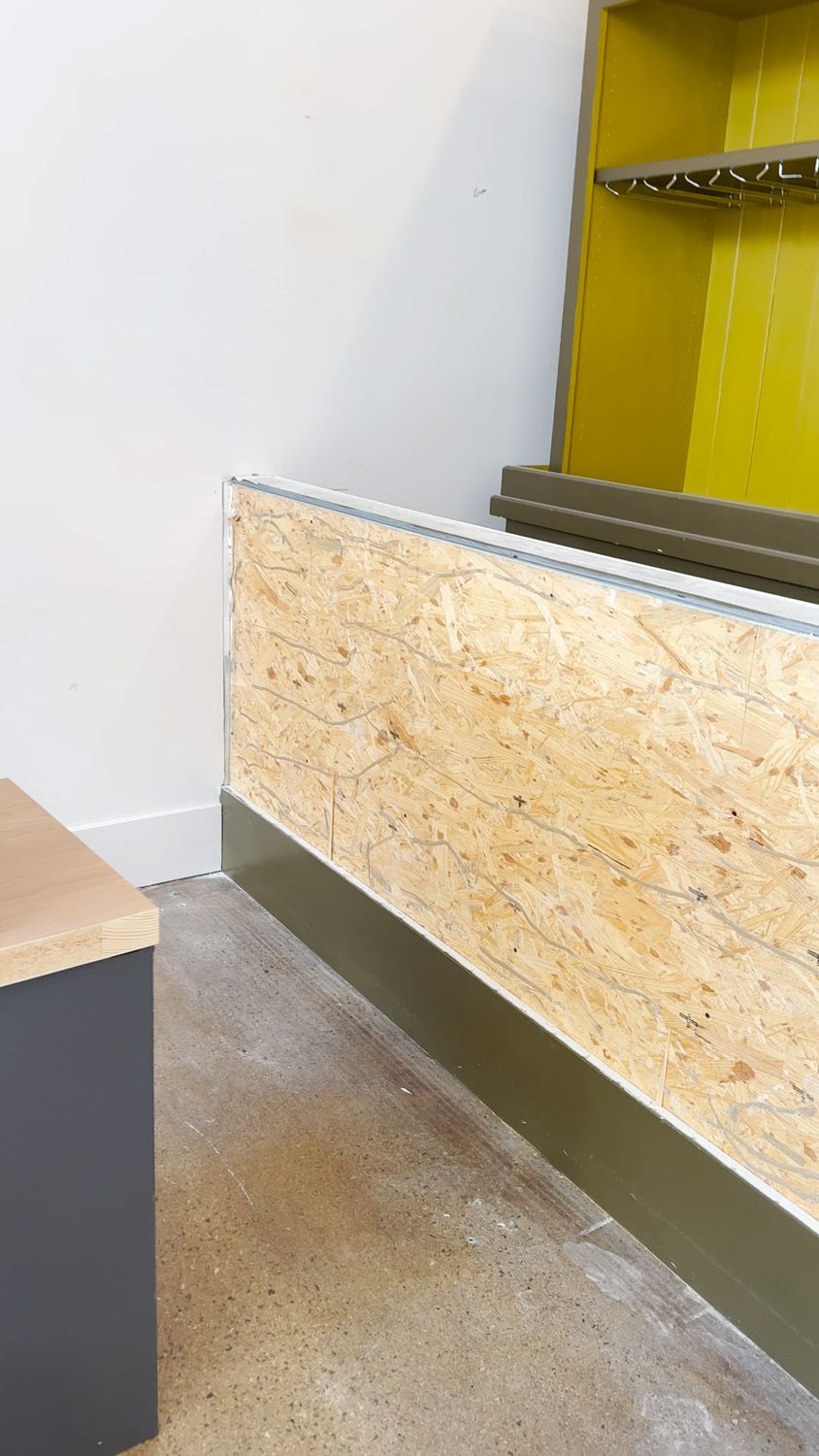 Empty retail counter with plywood front panel, gray floor, and yellow shelving in the background