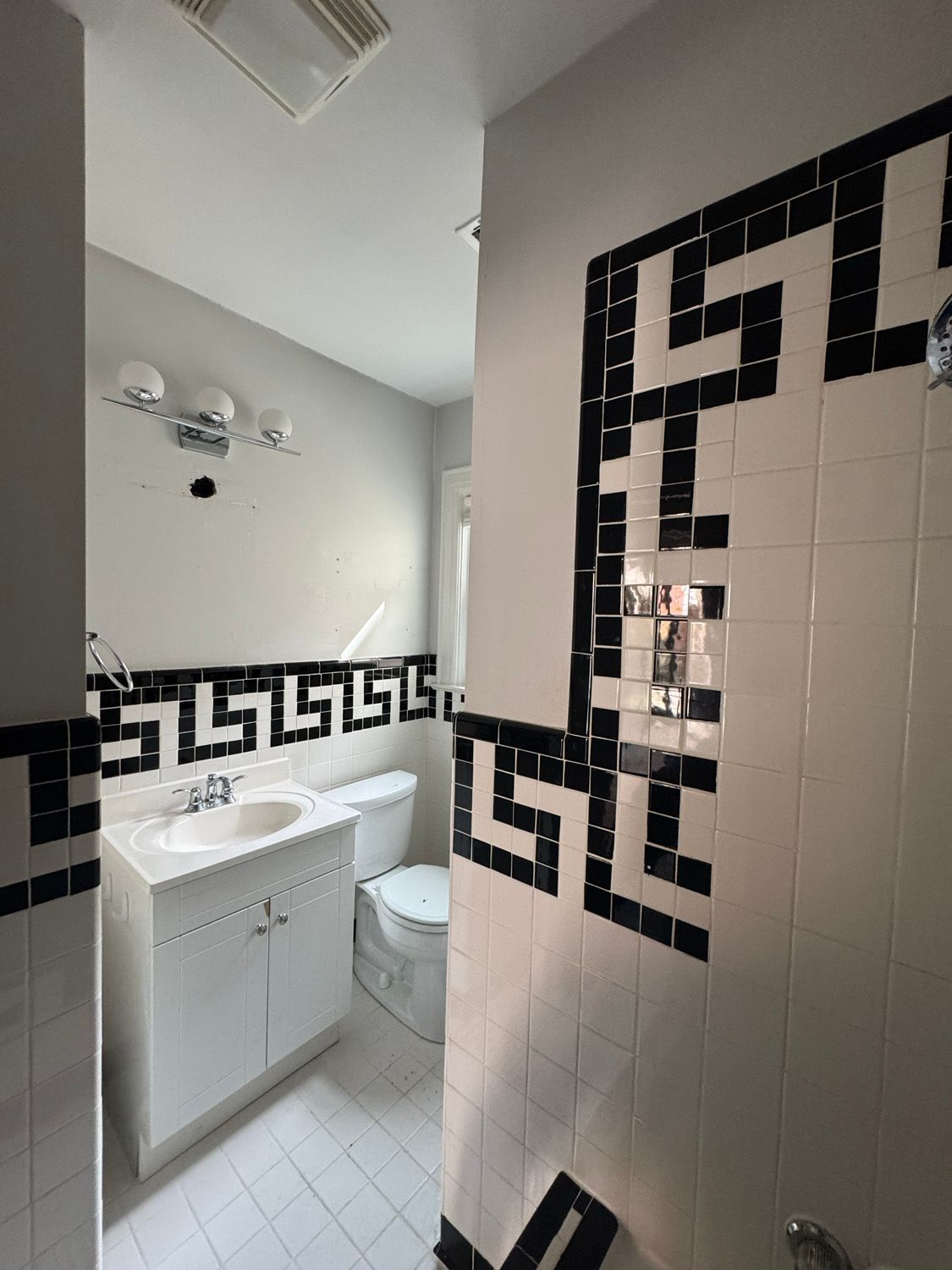 Small bathroom with white sink and toilet, black geometric tile border, and shower curtain partially visible.