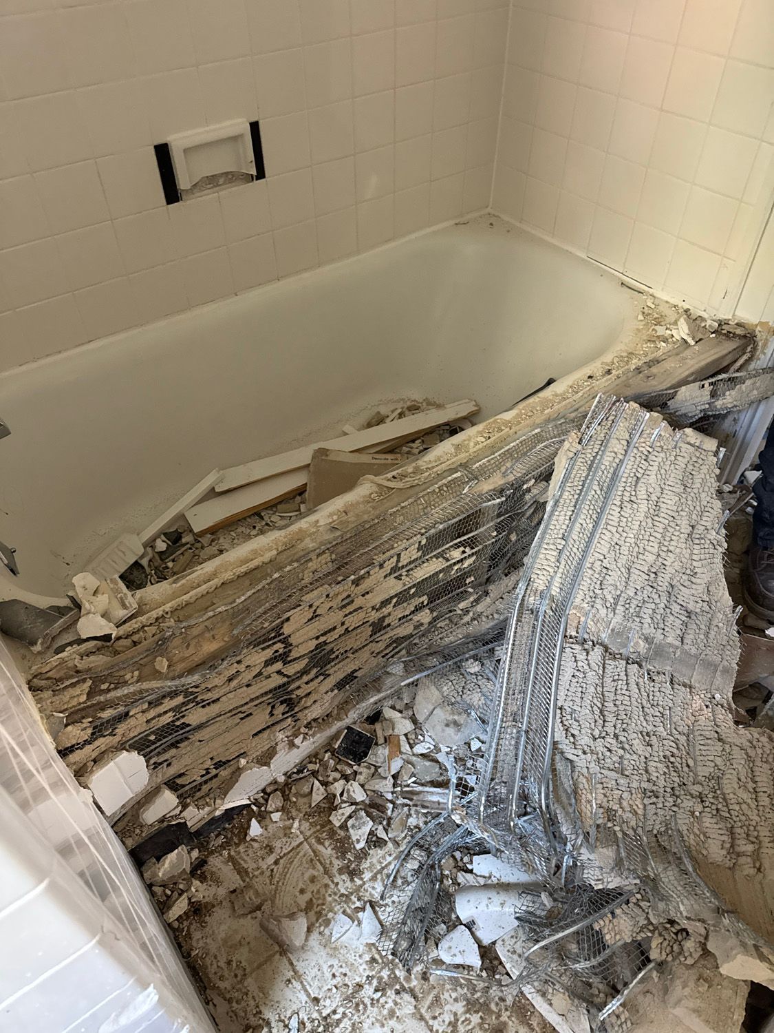 Bathtub filled with collapsed drywall debris and torn insulation in a damaged bathroom