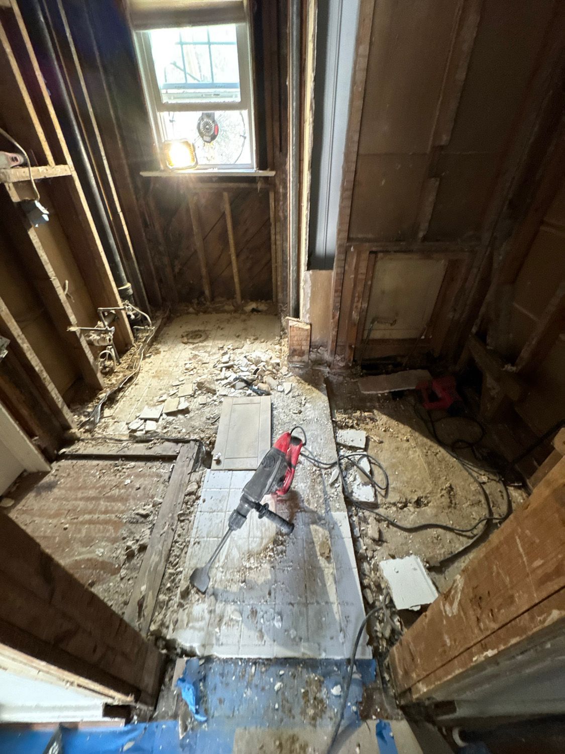 Partially demolished room with exposed floor joists, debris, and a red tool near a window.