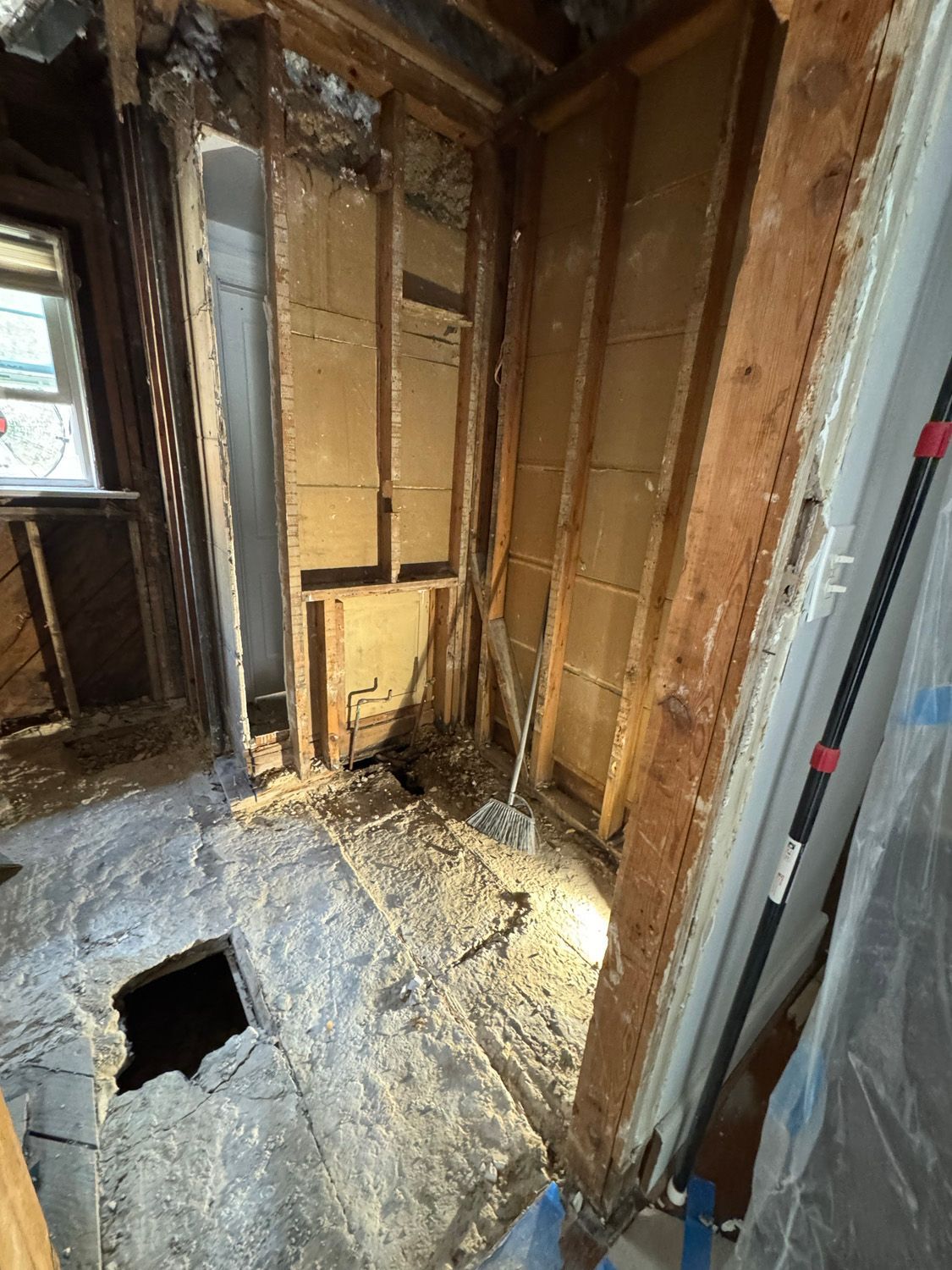 Damaged house interior with exposed framing, debris on the floor, and a hole in the floorboard