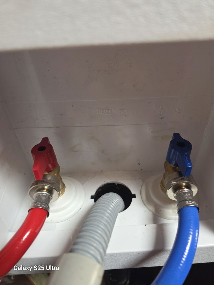 Red and blue water supply valves with a drain hose in a recessed laundry box.