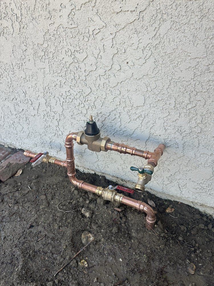 Copper water pipes and valves against a stucco wall, in dirt.