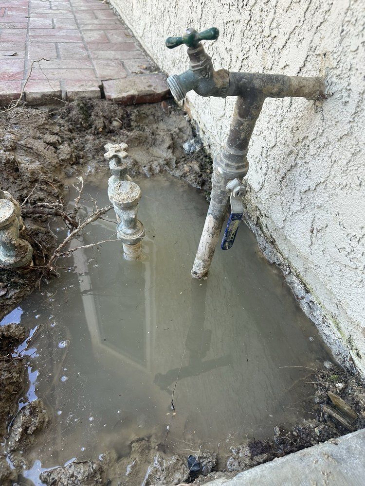 A muddy area with standing water around outdoor water spigots on a stucco wall.
