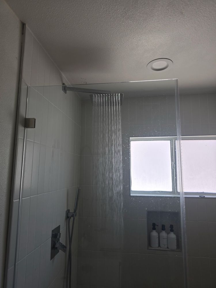 Shower with glass doors, water cascading, tile walls, and a small window.