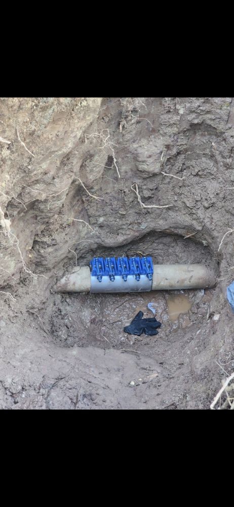 A pipe in a hole in the ground, sealed with blue clamps.
