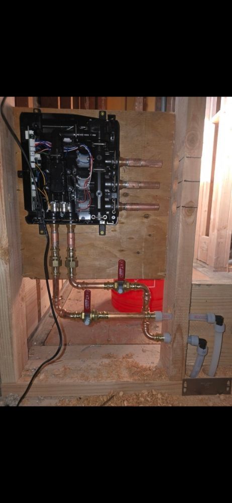 Plumbing system with a black box, copper pipes, and a red component on wooden support.