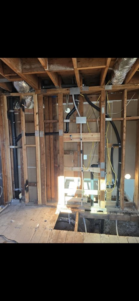 Interior view of a room under construction, showing exposed framing, electrical, and plumbing.