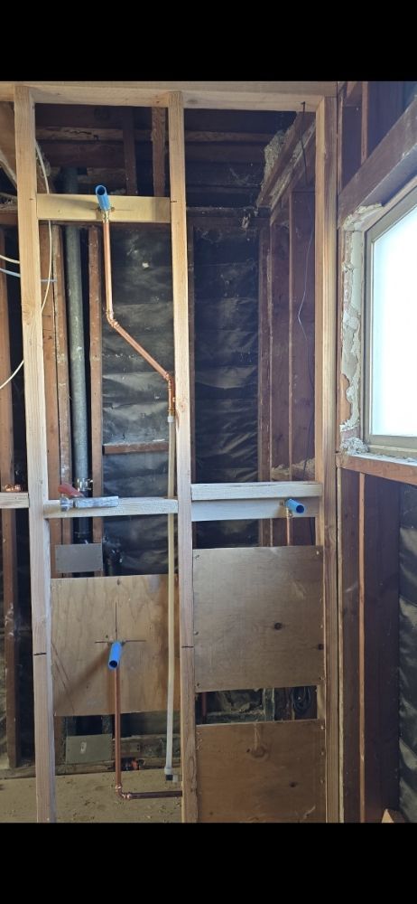 Interior framing of a bathroom renovation with exposed plumbing and plywood.