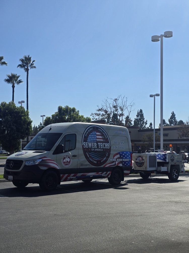 A white van with a trailer, parked on a sunny day. The van has a patriotic logo: 