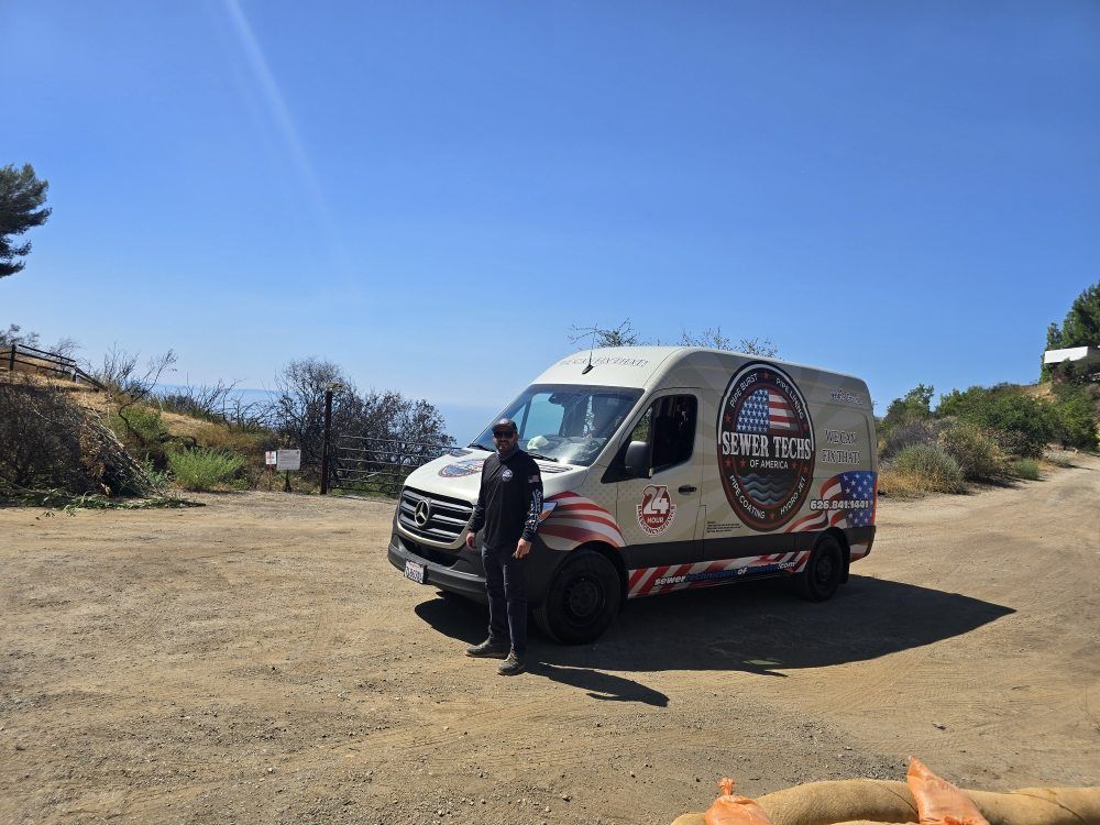 Man stands next to a van with a patriotic design on a dirt road with a blue sky.