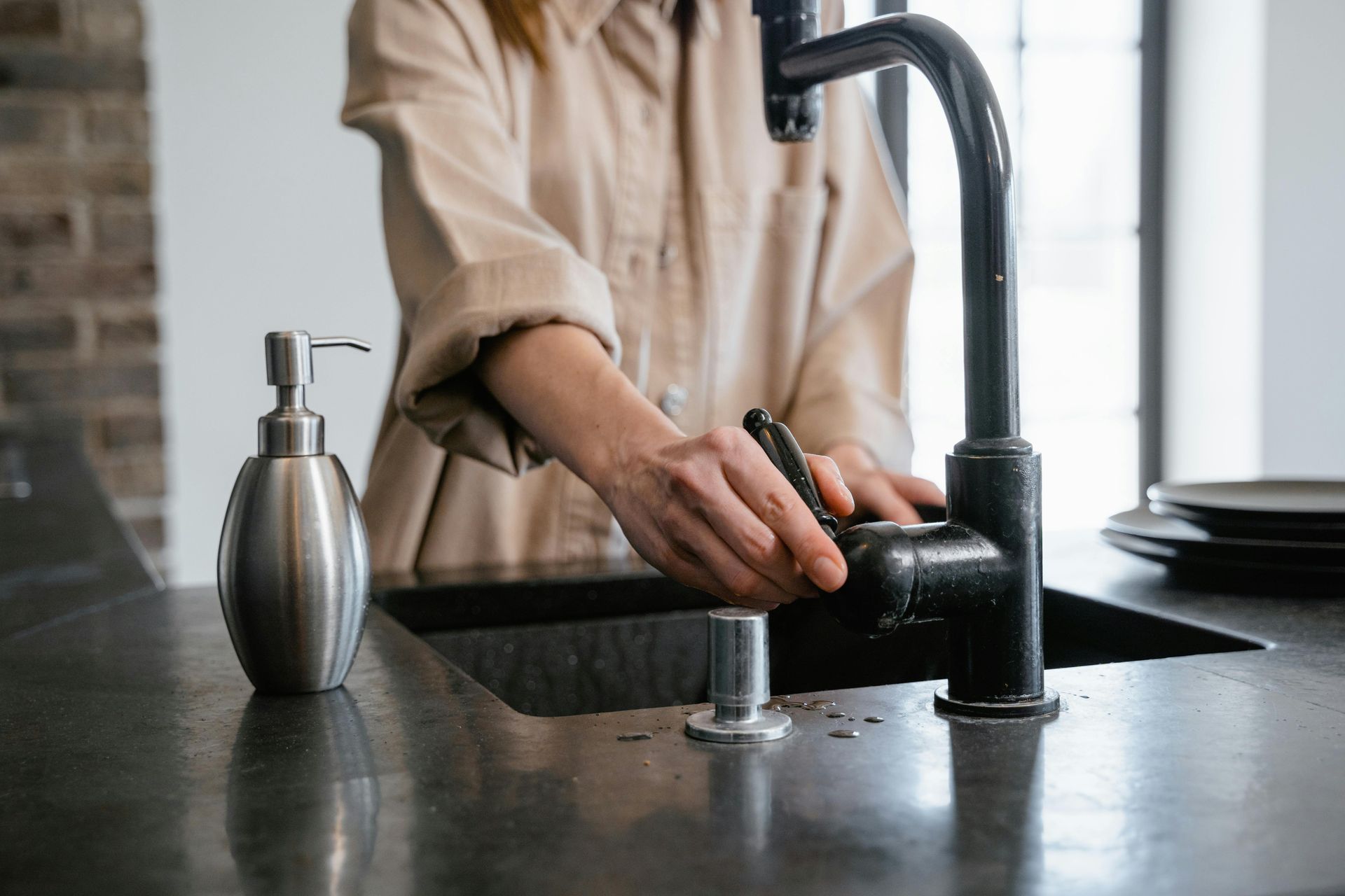 Person turns on a black faucet in a kitchen sink, soap dispenser nearby.