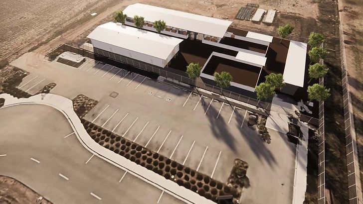 Aerial view of a modern building with a large parking lot. White roof and dark exterior with trees.