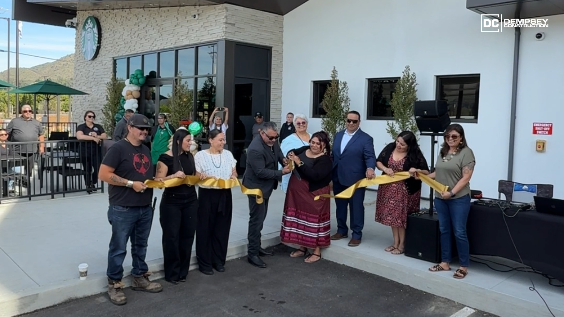 A group of people standing in front of a building holding a gold ribbon during a ceremonial ribbon-cutting event.
