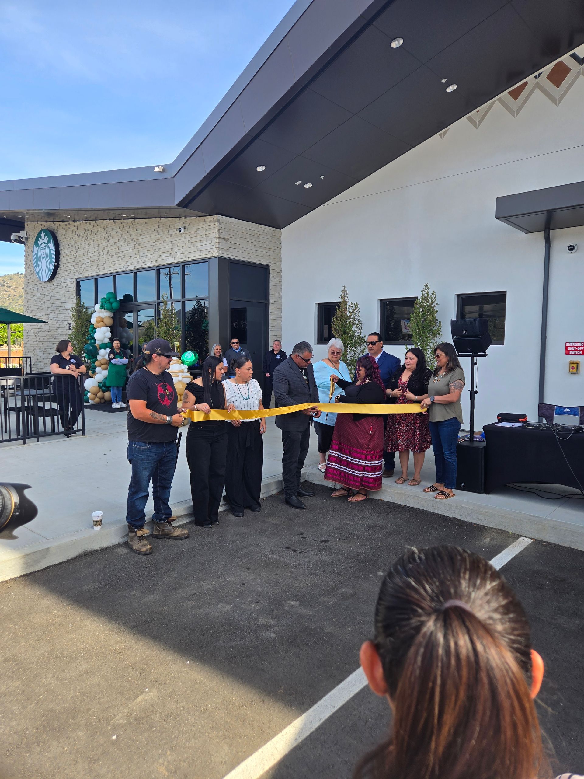 A group of people standing in front of a new Starbucks building, cutting a ceremonial gold ribbon together.