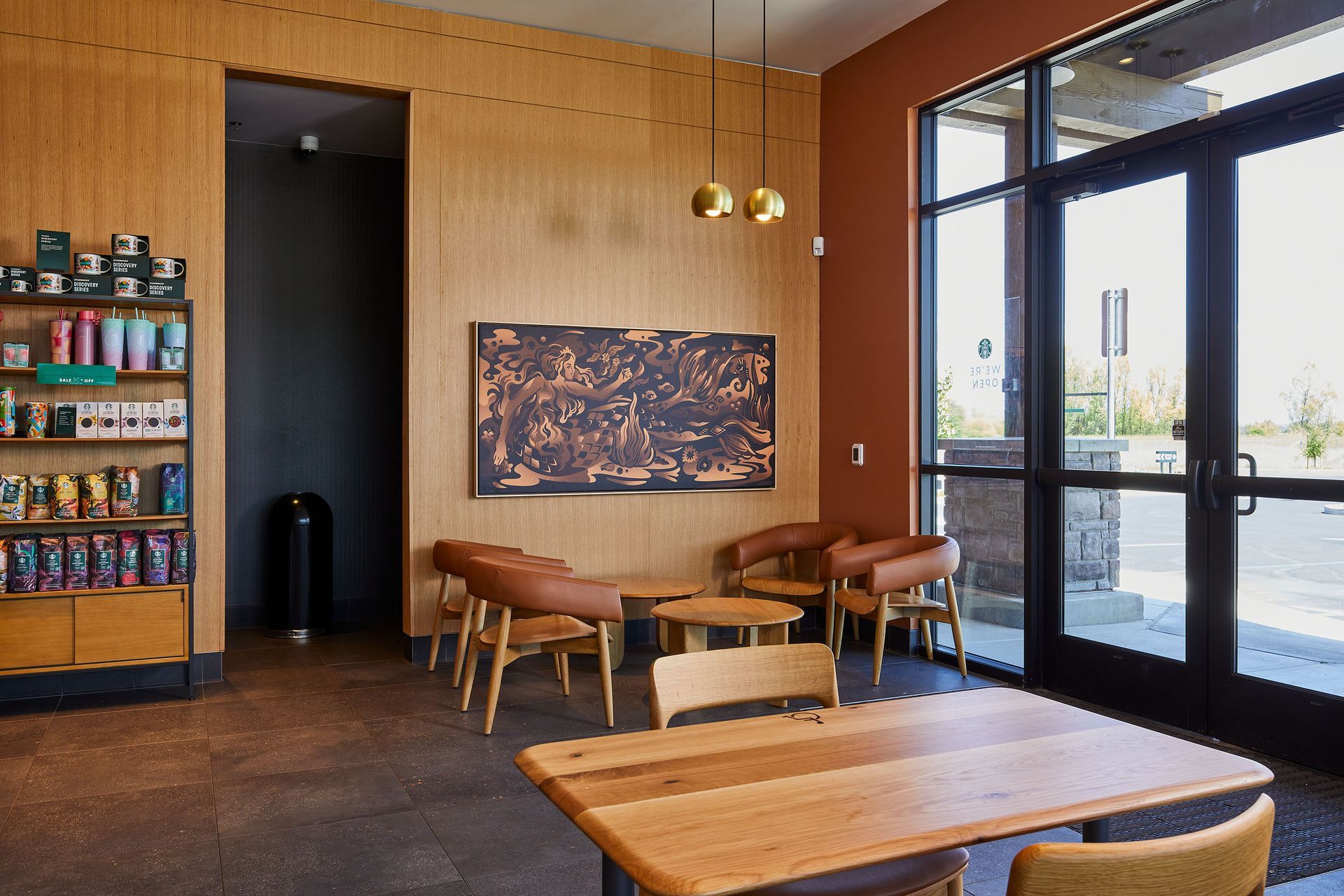 Cozy café interior with wooden tables, tan chairs, wall art, and large glass entrance doors