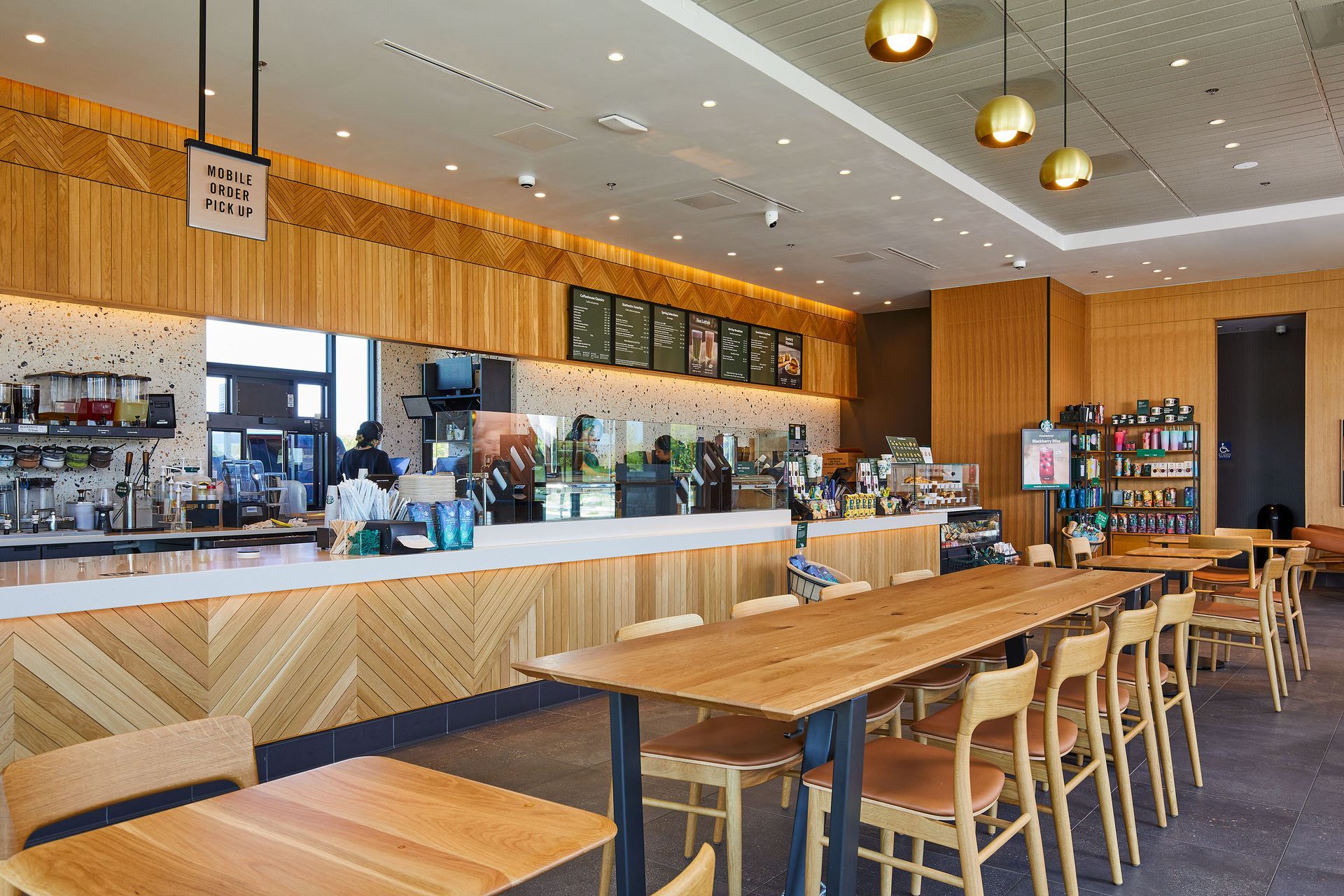 Modern café interior with wooden tables, stools, and a long white counter under warm pendant lights