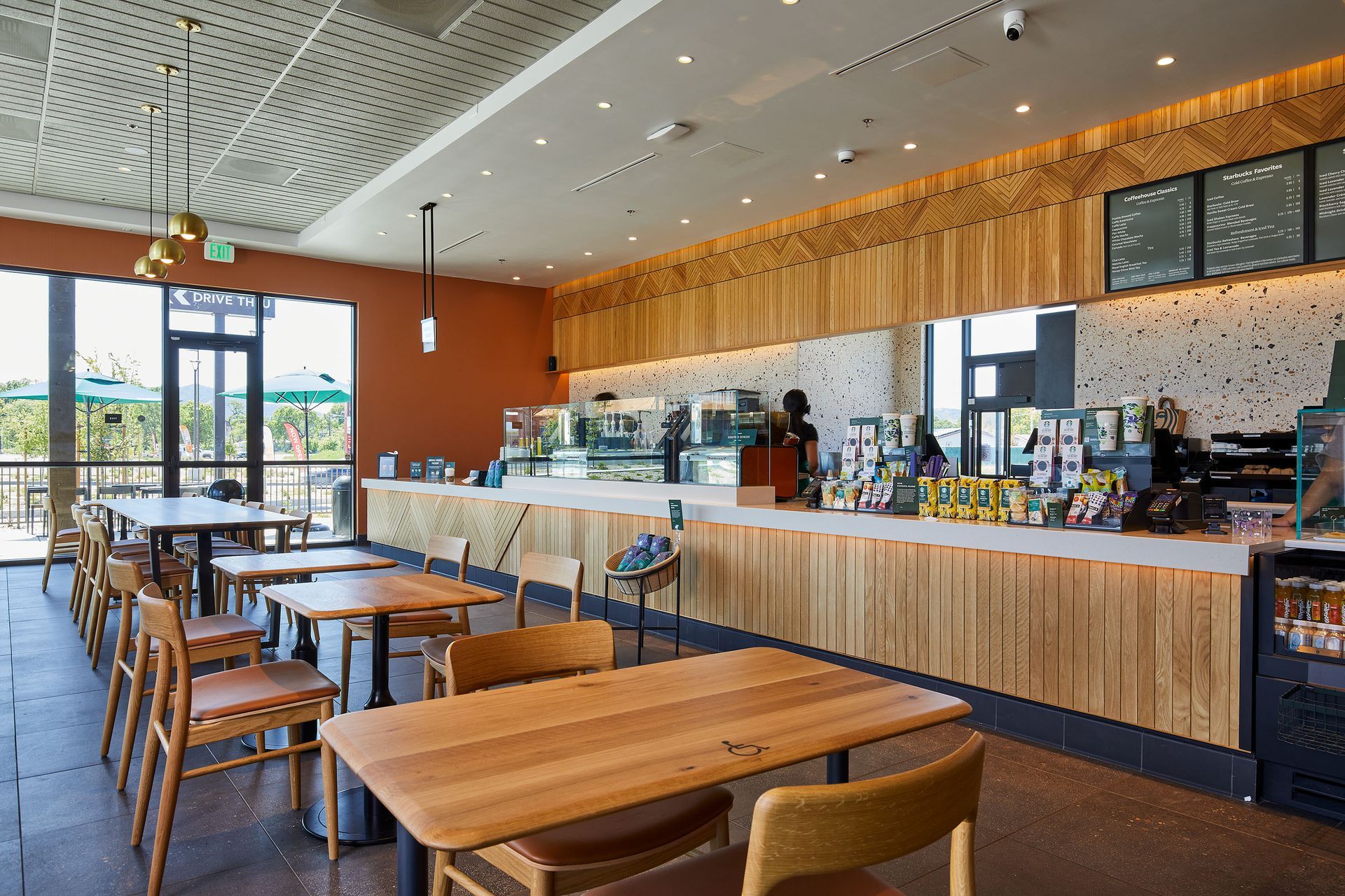 Empty modern café with wooden tables, long counter, and bright windows.