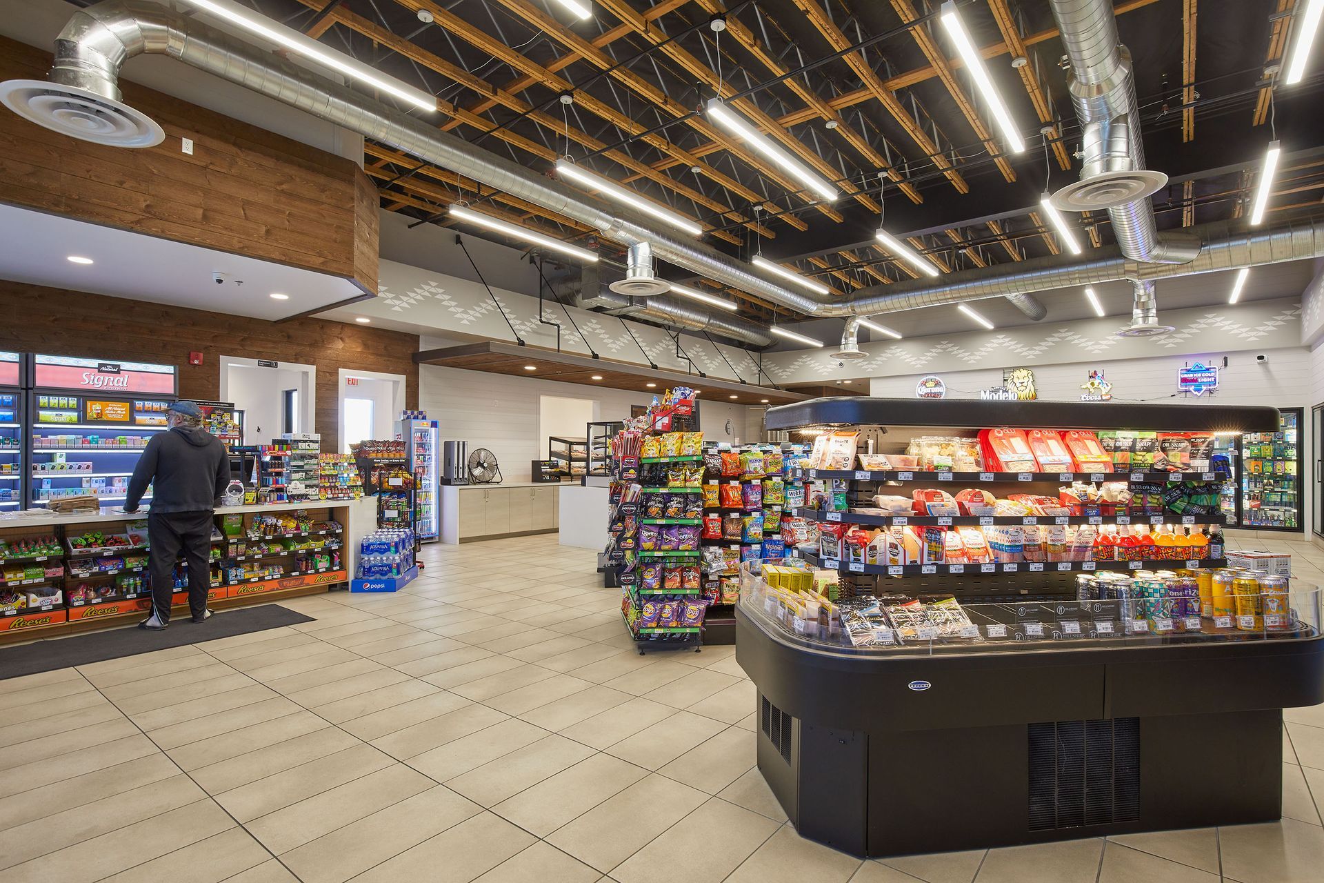Convenience store interior with snack displays, refrigerators, and a customer browsing near the left wall