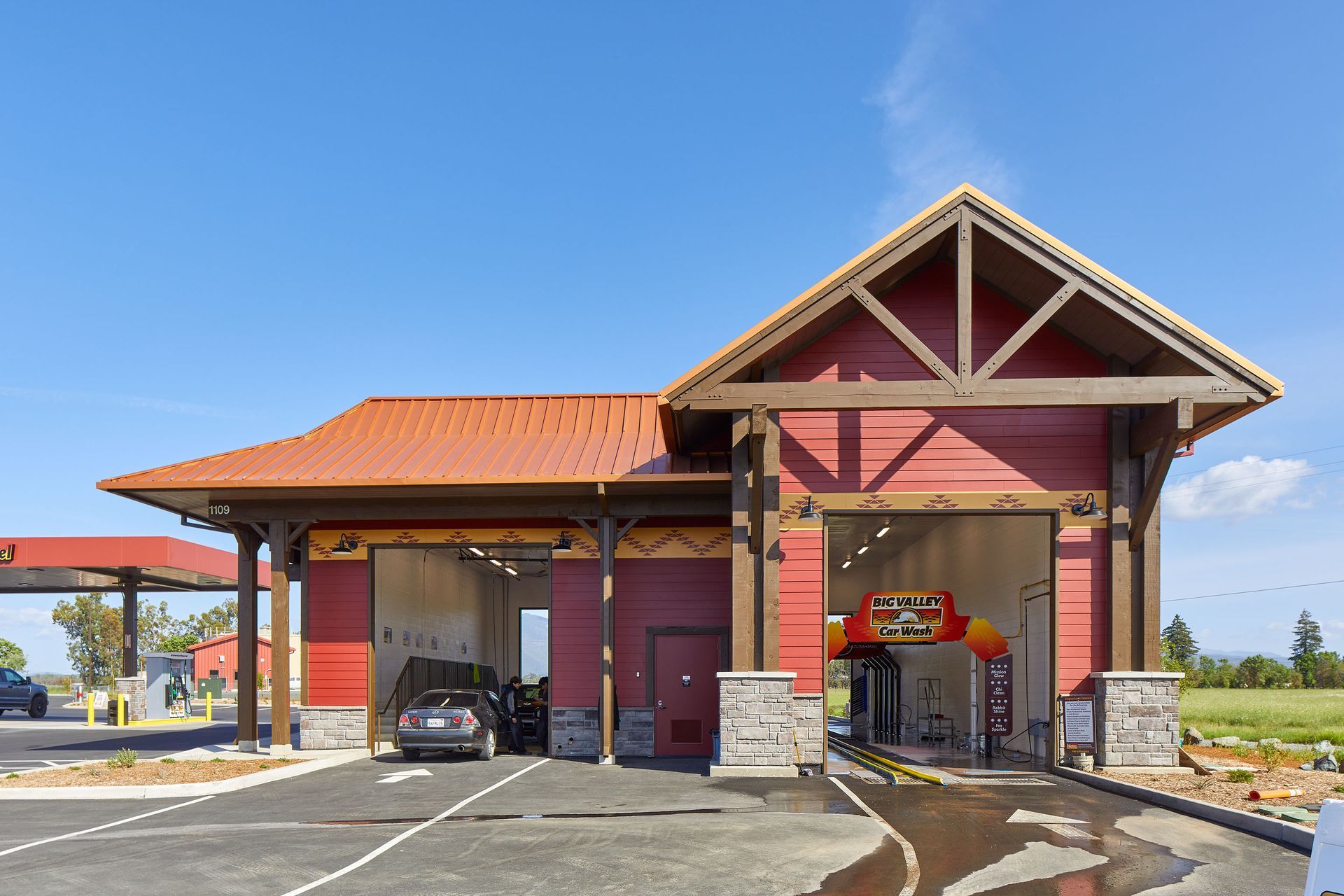Gas station car wash with red-roofed building and a car in one bay under a blue sky