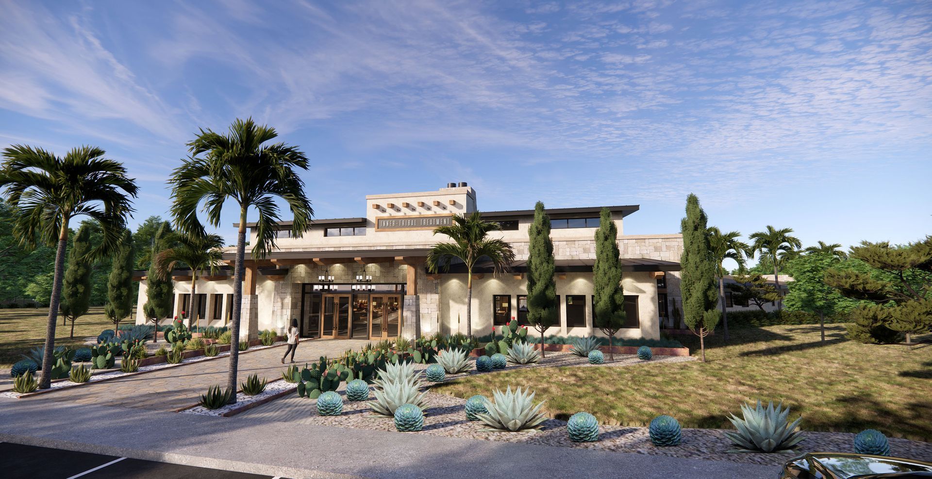 A modern, light-colored building with a stone exterior and flat roof, surrounded by desert landscaping and palm trees.