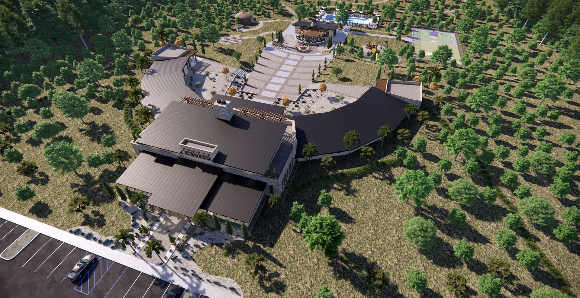 Aerial view of a large modern building complex with parking, surrounded by green trees in a natural landscape.