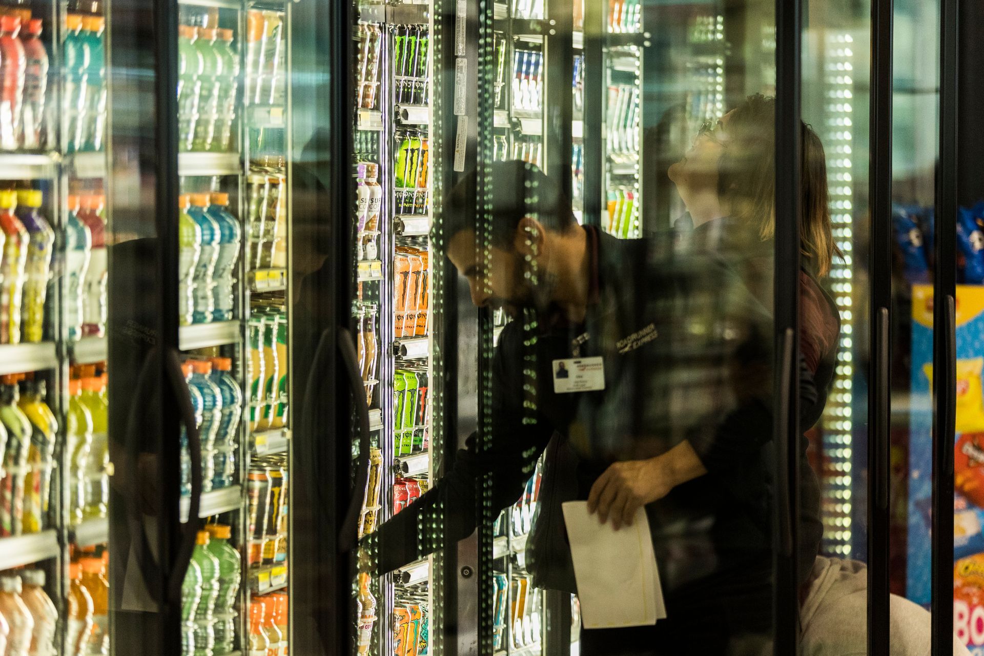 A man is standing in front of a refrigerator in a grocery store.