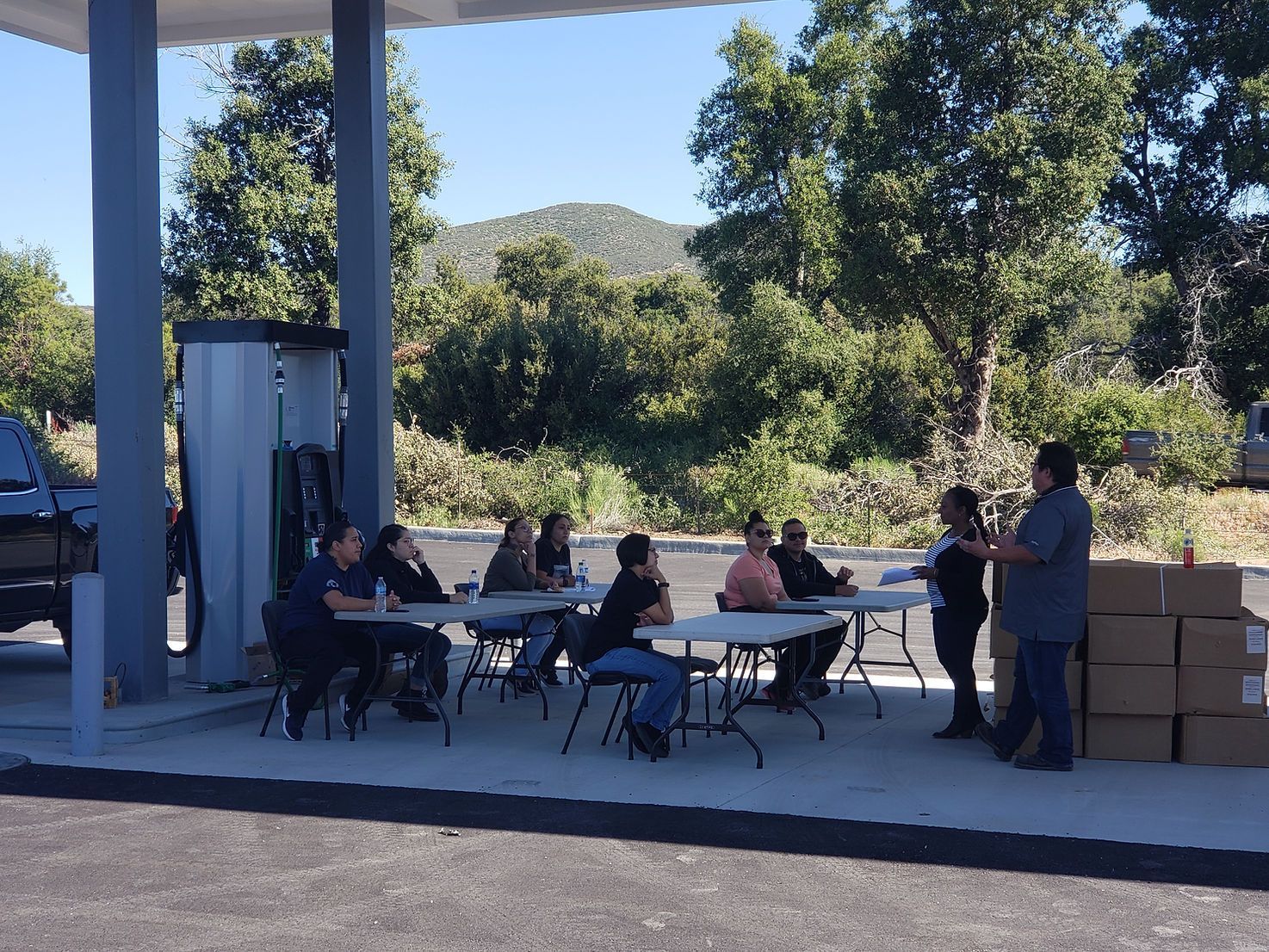 A group of people are sitting at tables outside of a gas station