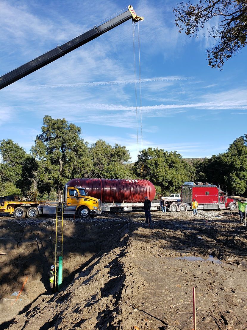 A crane is lifting a tanker truck in a dirt field.