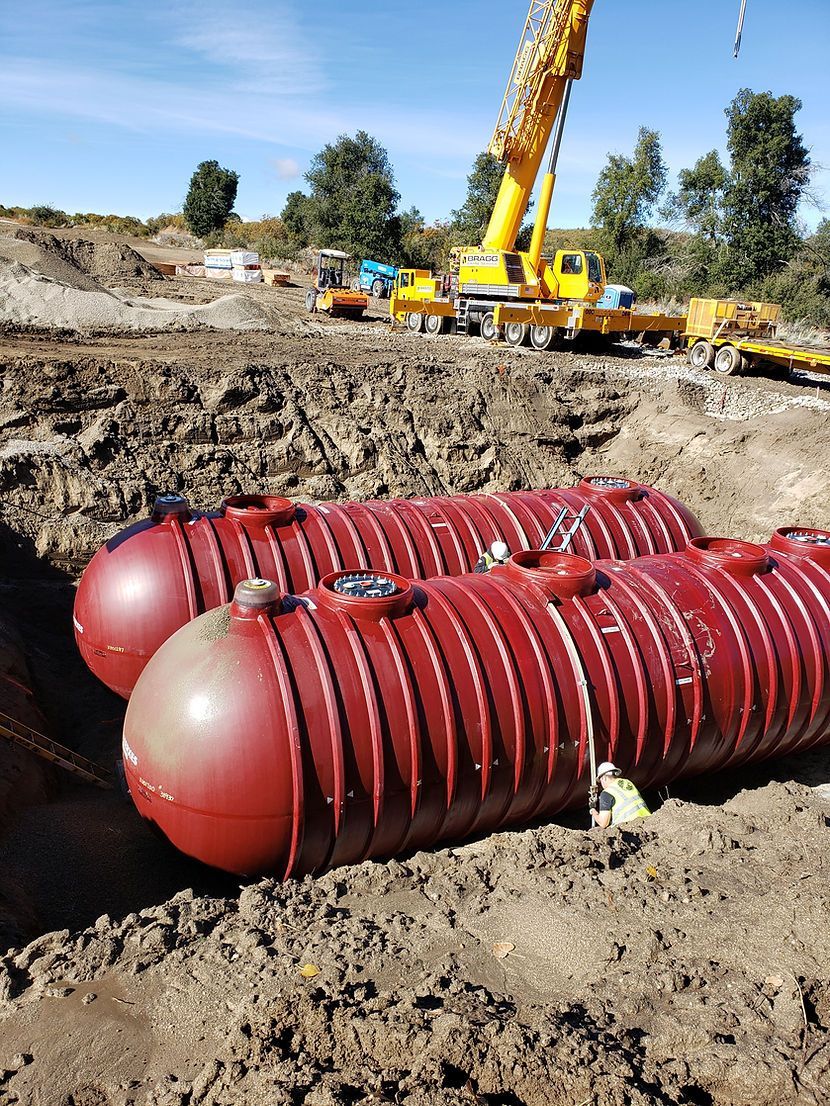 Two red tanks are sitting in the dirt on a construction site with a crane in the background.