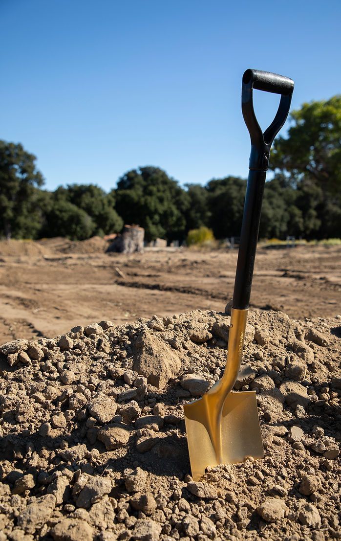 A gold shovel is sitting on top of a pile of dirt.