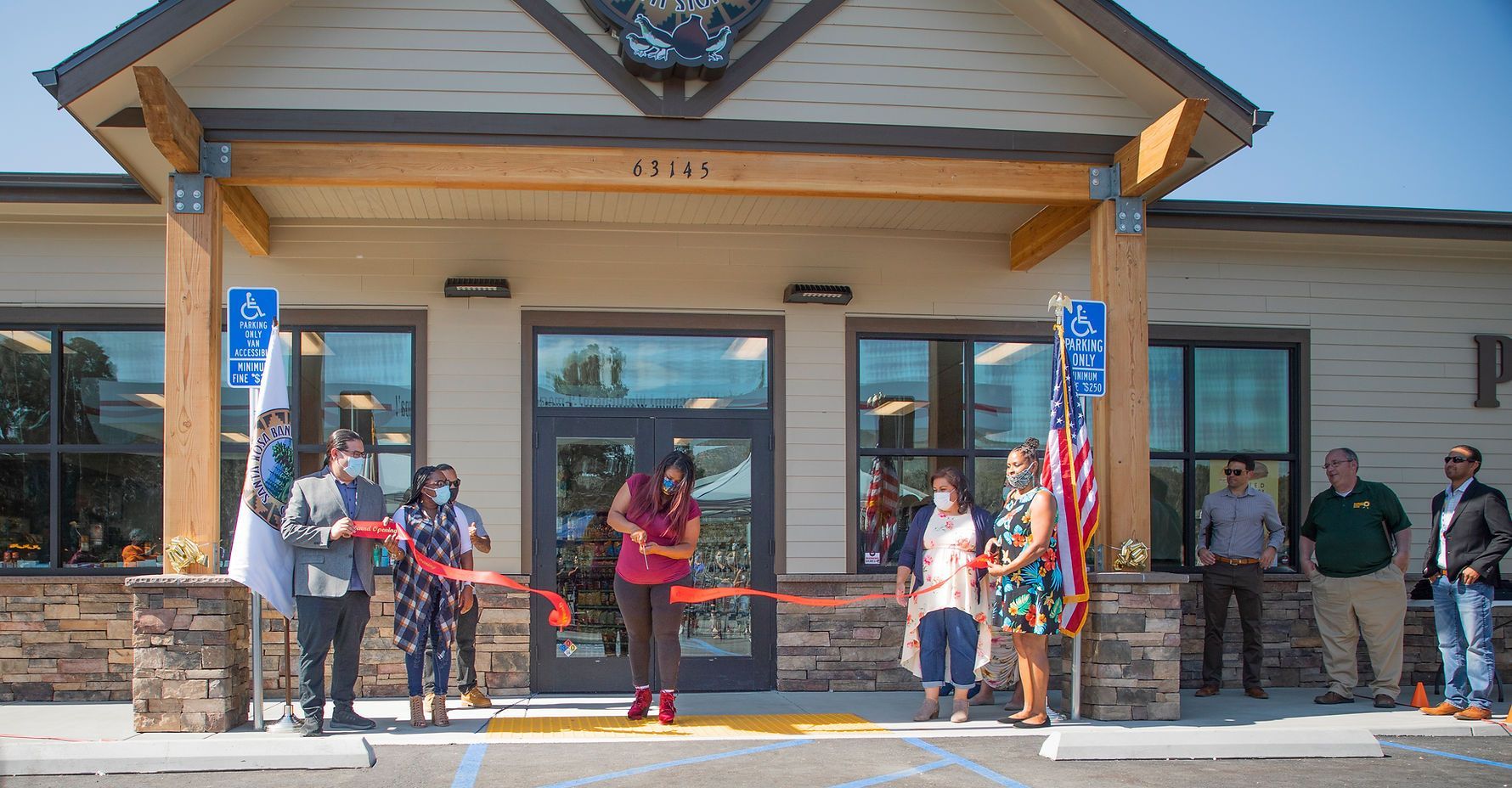 A group of people are cutting a red ribbon in front of a building.