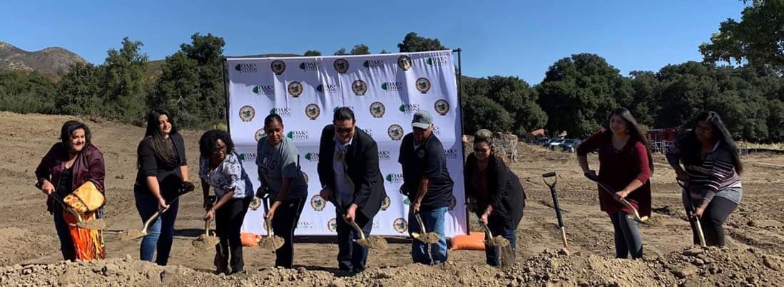 A group of people are standing in a field holding shovels.
