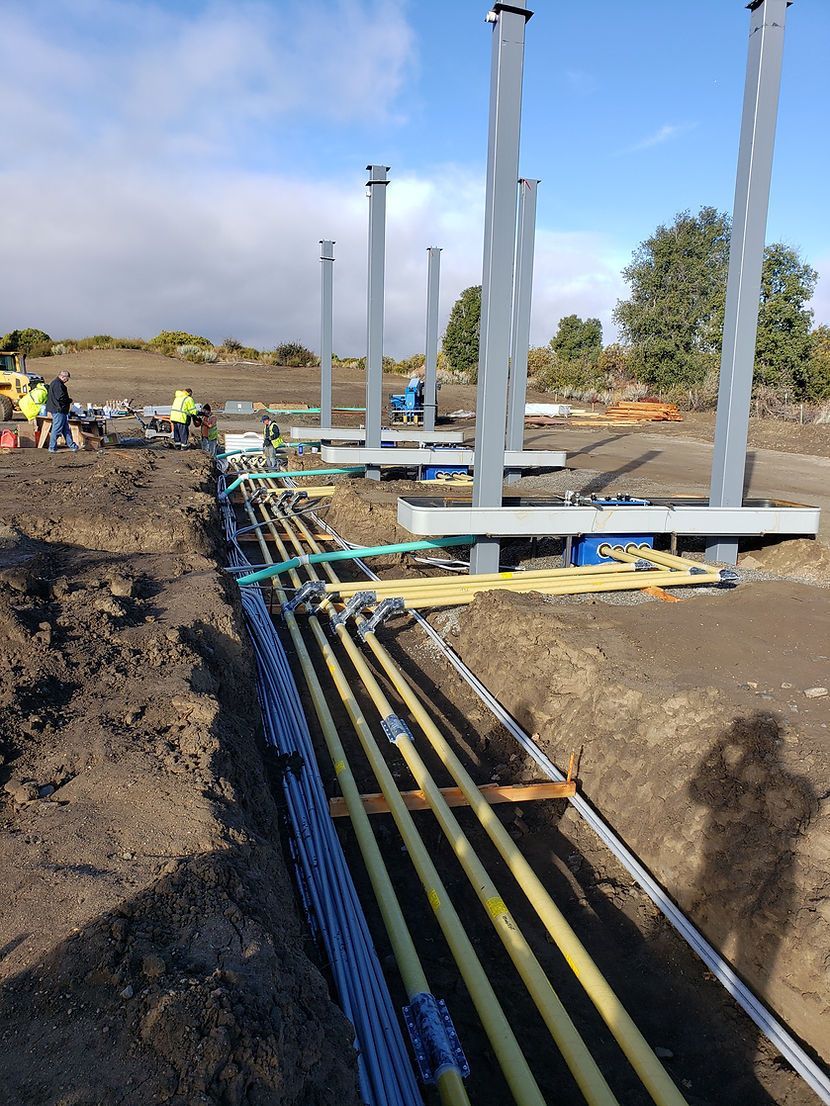 A row of yellow pipes are laying in the dirt on a construction site.
