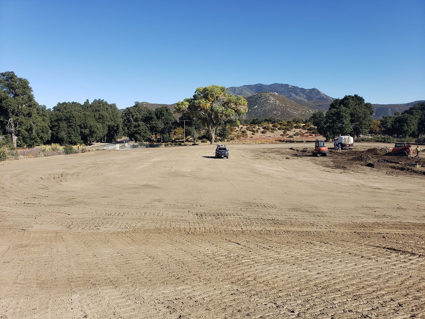 A large dirt field with trees and mountains in the background.