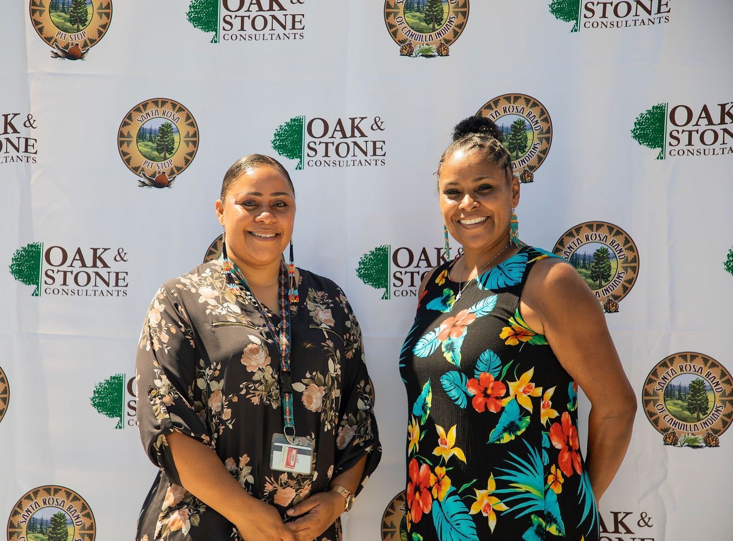 Two women are posing for a picture in front of a backdrop that says oak & stone