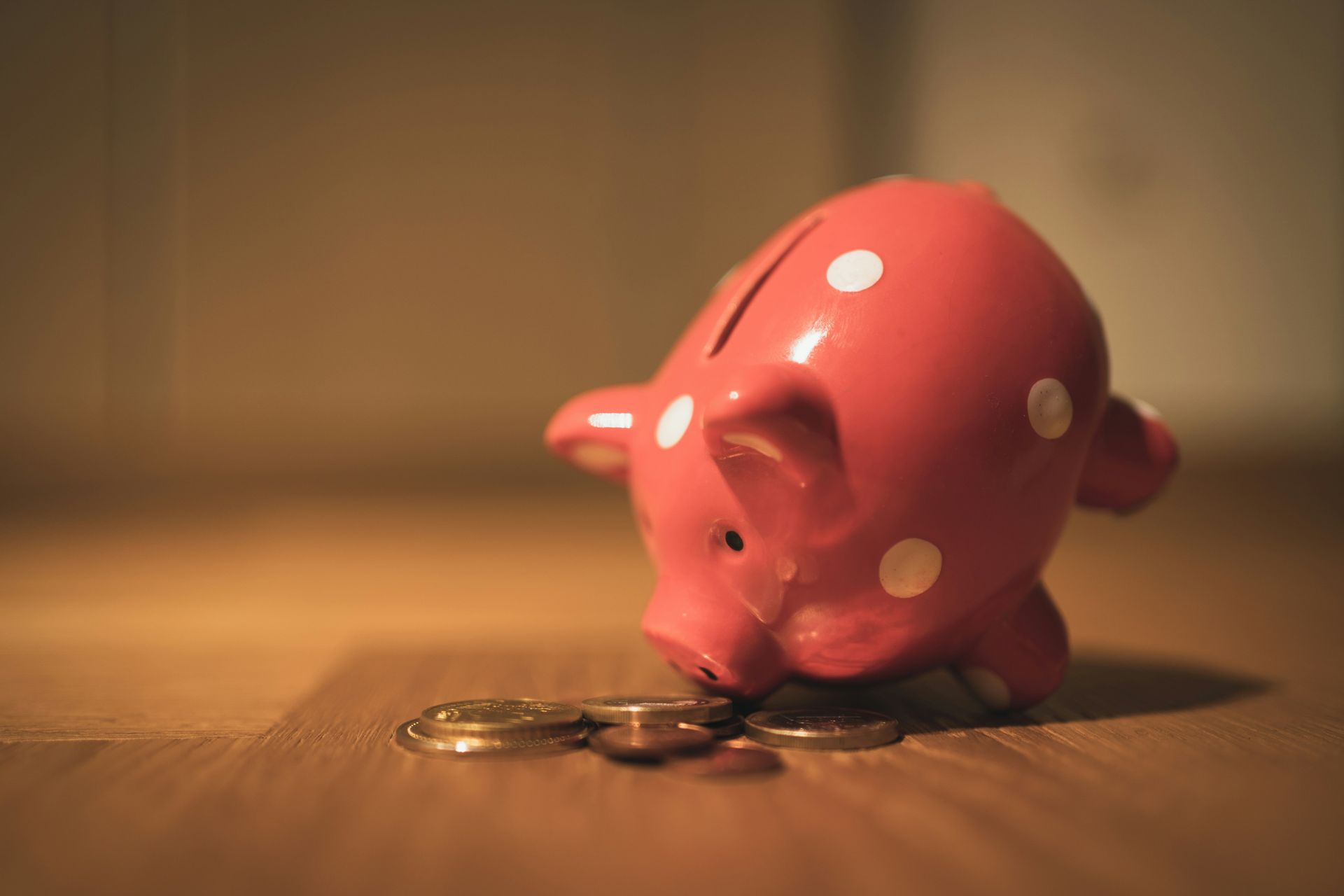 Pink piggy bank tipped over, coins spilling out onto a wooden floor.