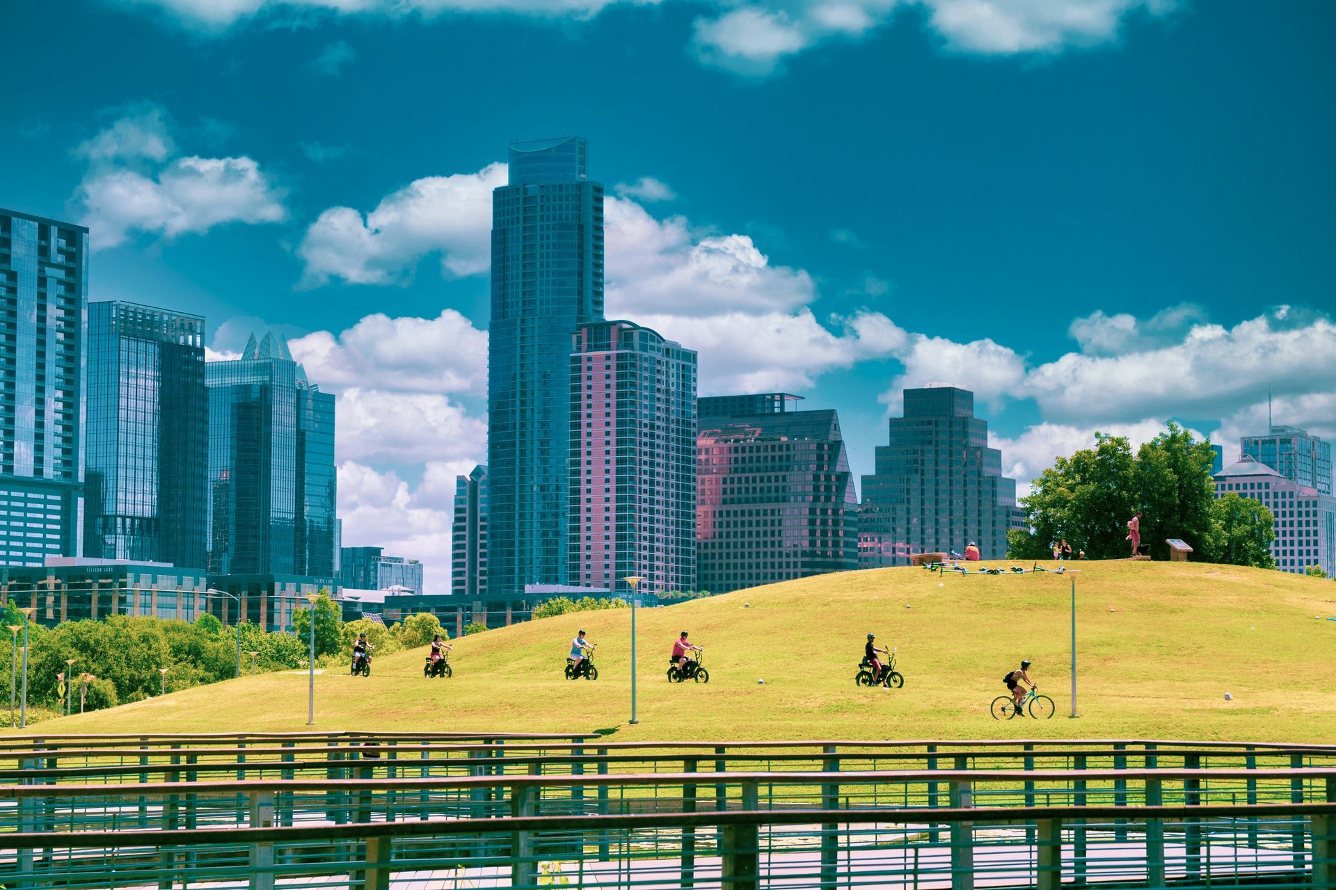 Green hill in a park with cyclists and city skyline on a sunny day with blue sky and white clouds.