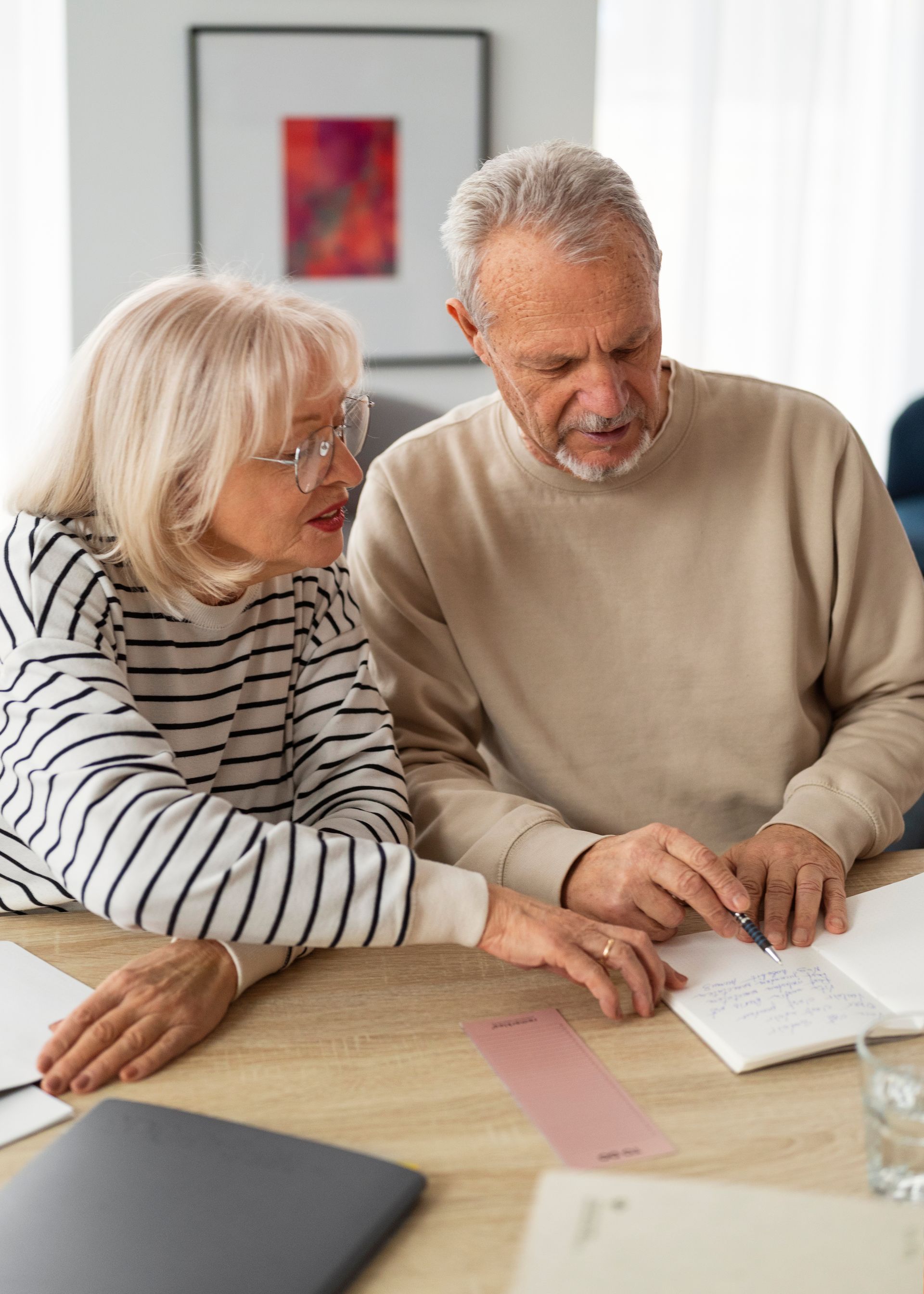 Elderly couple reviewing paperwork at a table, both focused and engaged, indoors.