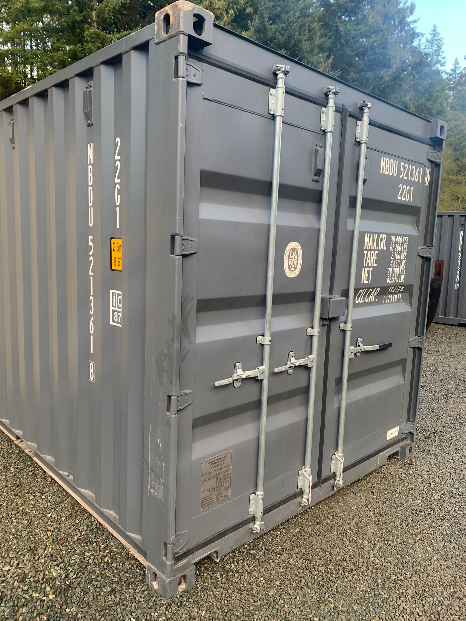 A gray shipping container is sitting on top of a gravel lot.