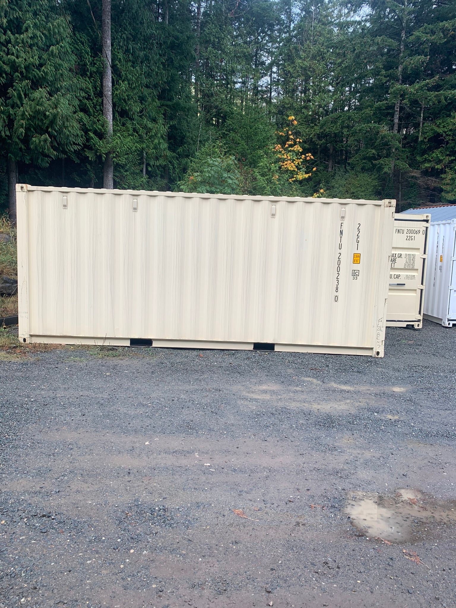 A shipping container is sitting in a gravel lot in front of a forest.