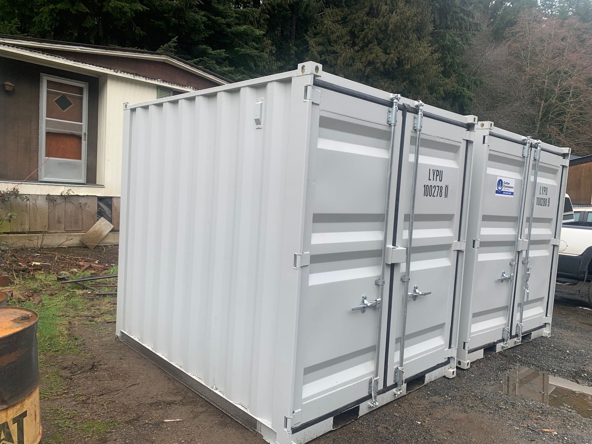 A white shipping container is parked in front of a house.