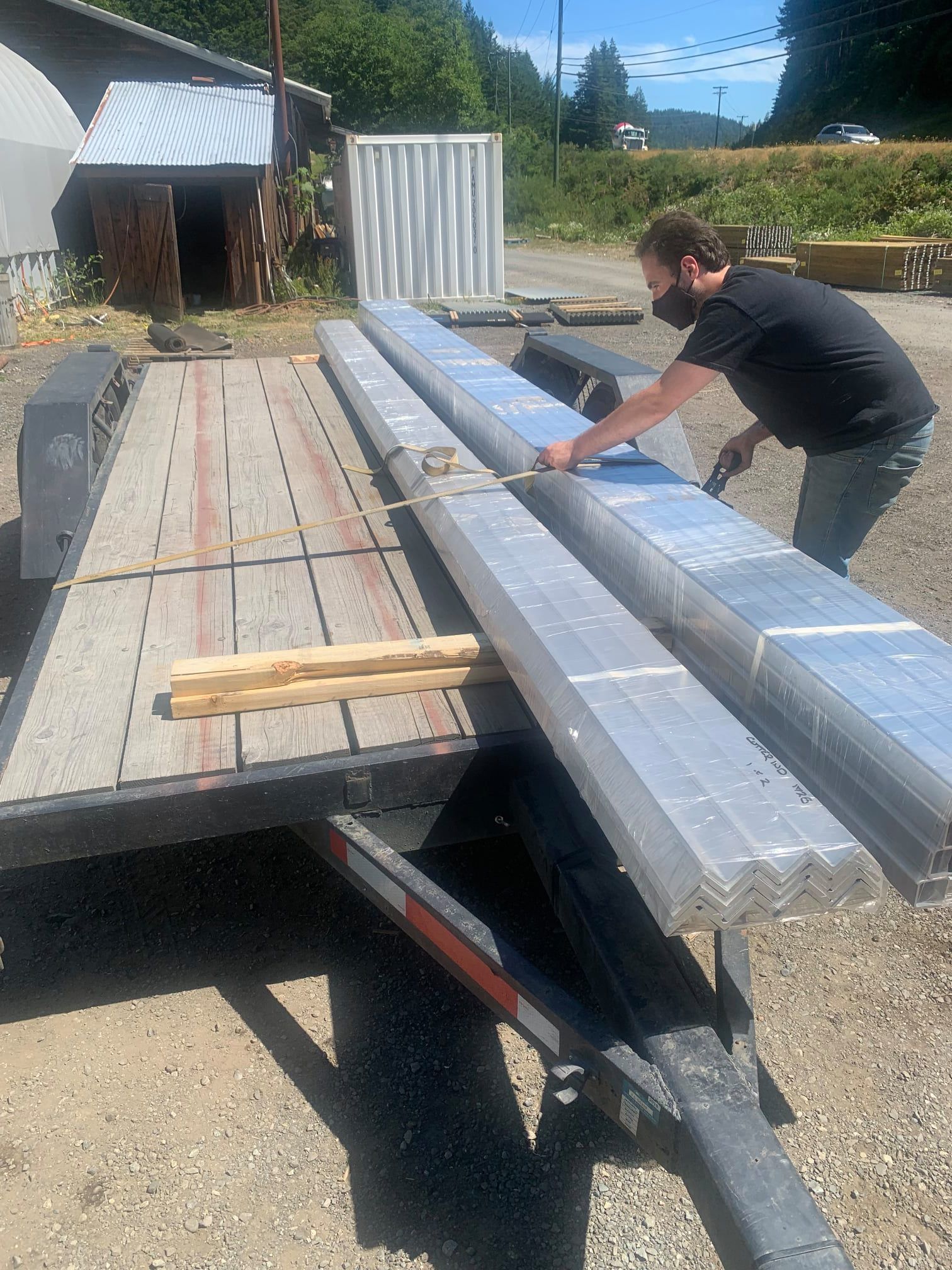 Person loading long wrapped materials onto a flatbed trailer outdoors.