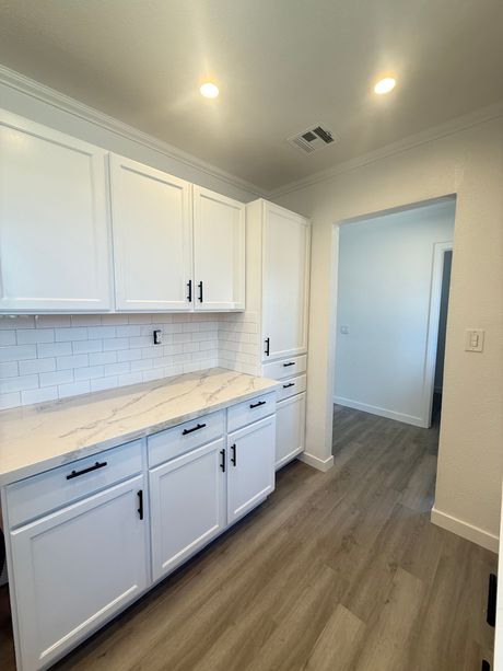 White kitchen cabinets with dark hardware, light countertops, and gray wood-look floors.