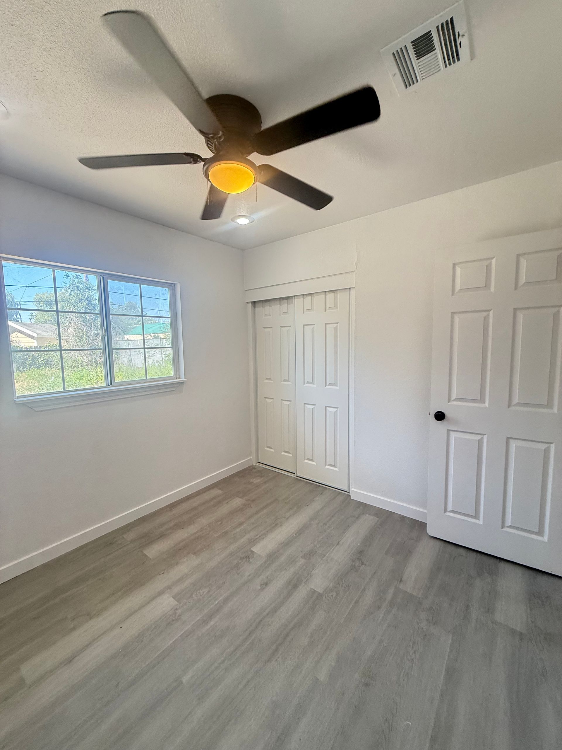 Empty room with gray flooring, white walls, a ceiling fan, window, and closed doors.